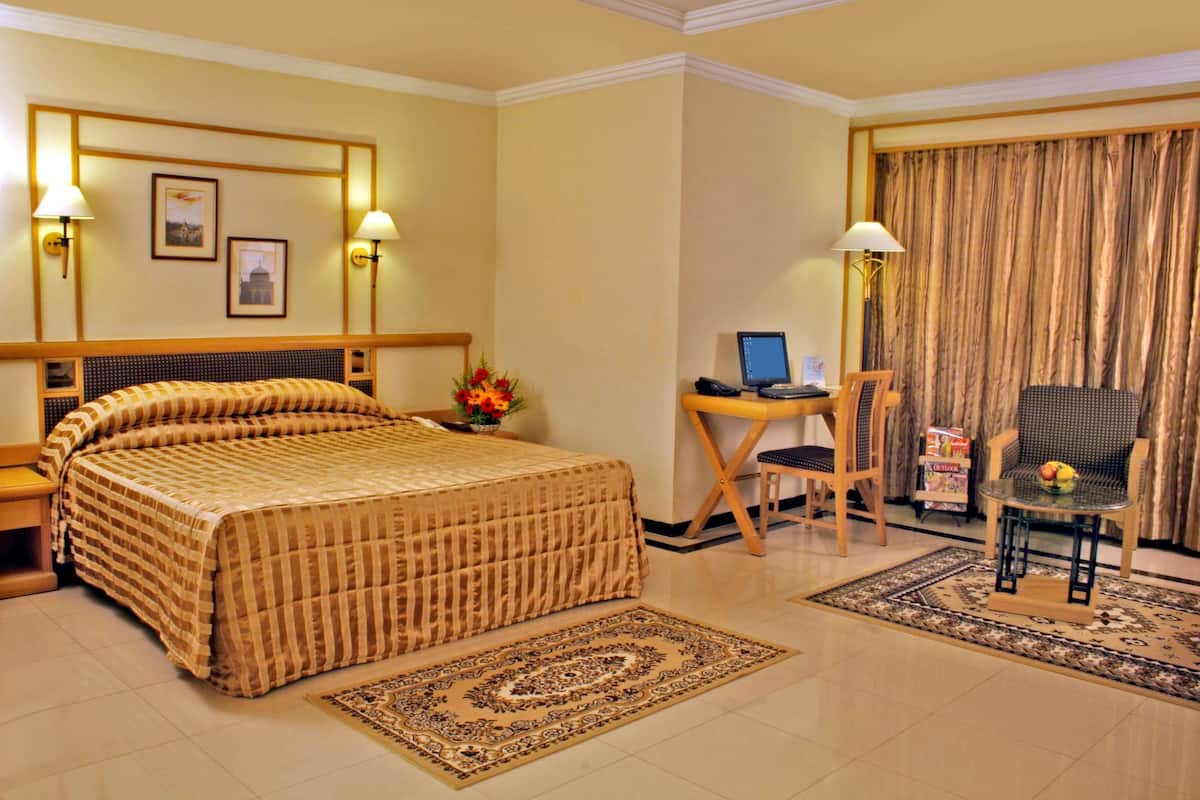 A hotel room with a large bed, a desk with a computer, a chair, and a small table with a fruit bowl.