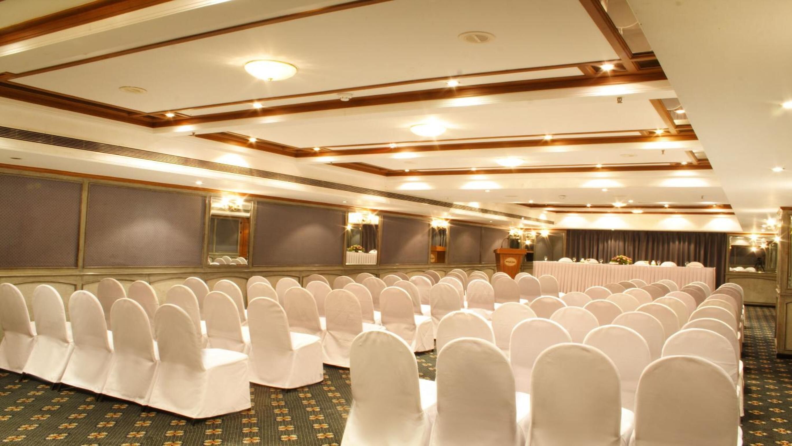 Un salón de conferencias con filas de sillas blancas, un atril y una zona de escenario.