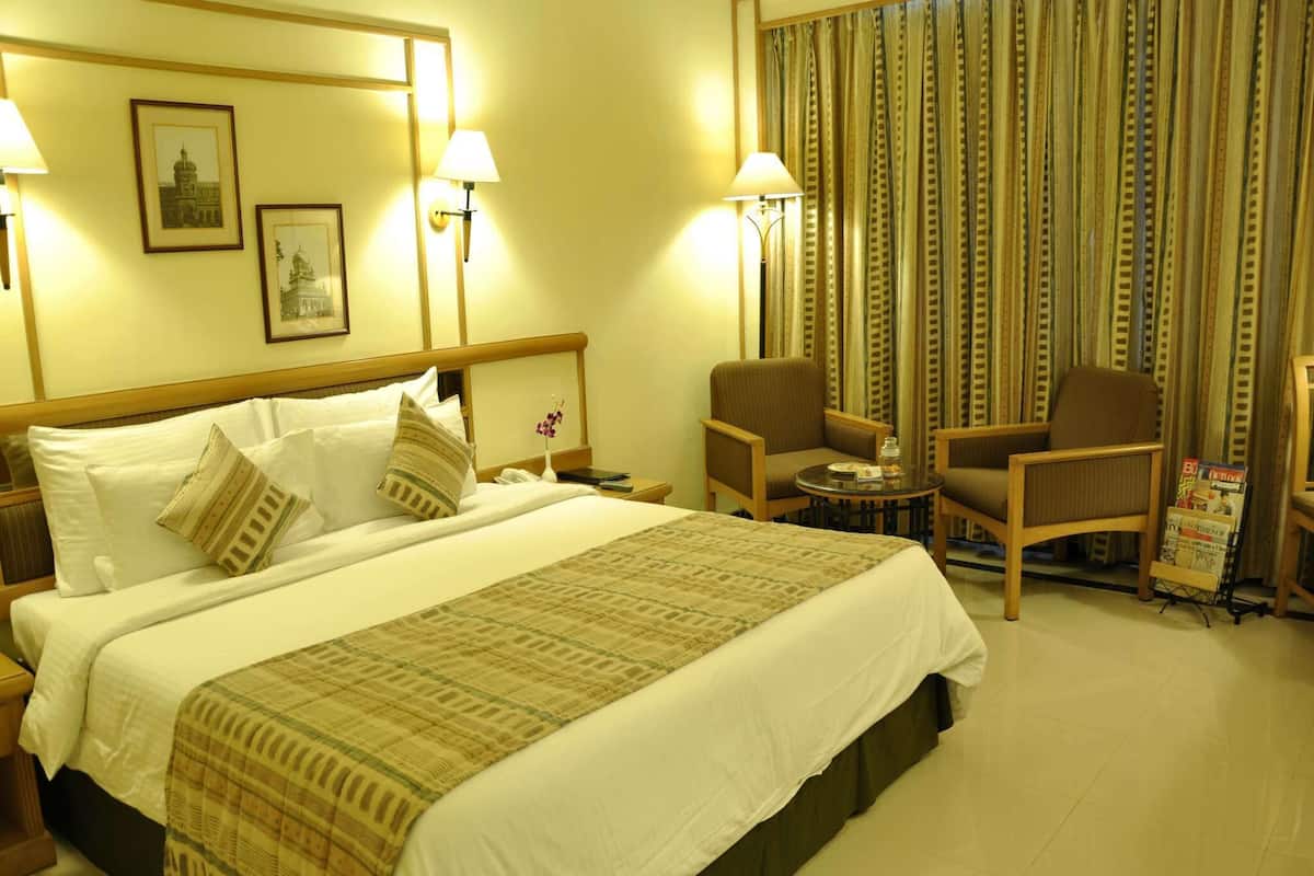 A hotel room with a large bed, two chairs, a small table, and a magazine rack.
