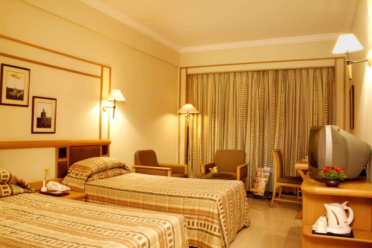A hotel room with two beds, a television, a coffee maker, and a desk with a lamp.