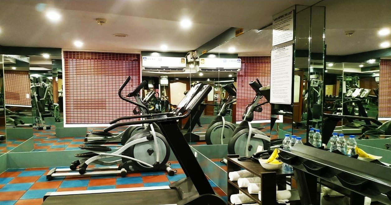 A gym with exercise equipment, mirrors, and a tiled floor.