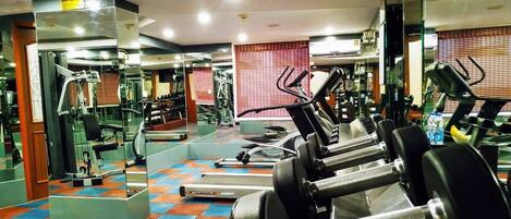 Un gimnasio con equipo de ejercicio, espejos y suelo de baldosas.