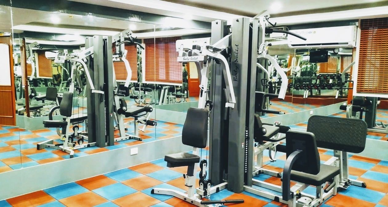 Une salle de sport équipée de divers appareils d’exercice, de miroirs et dotée d’un sol carrelé aux couleurs vives.