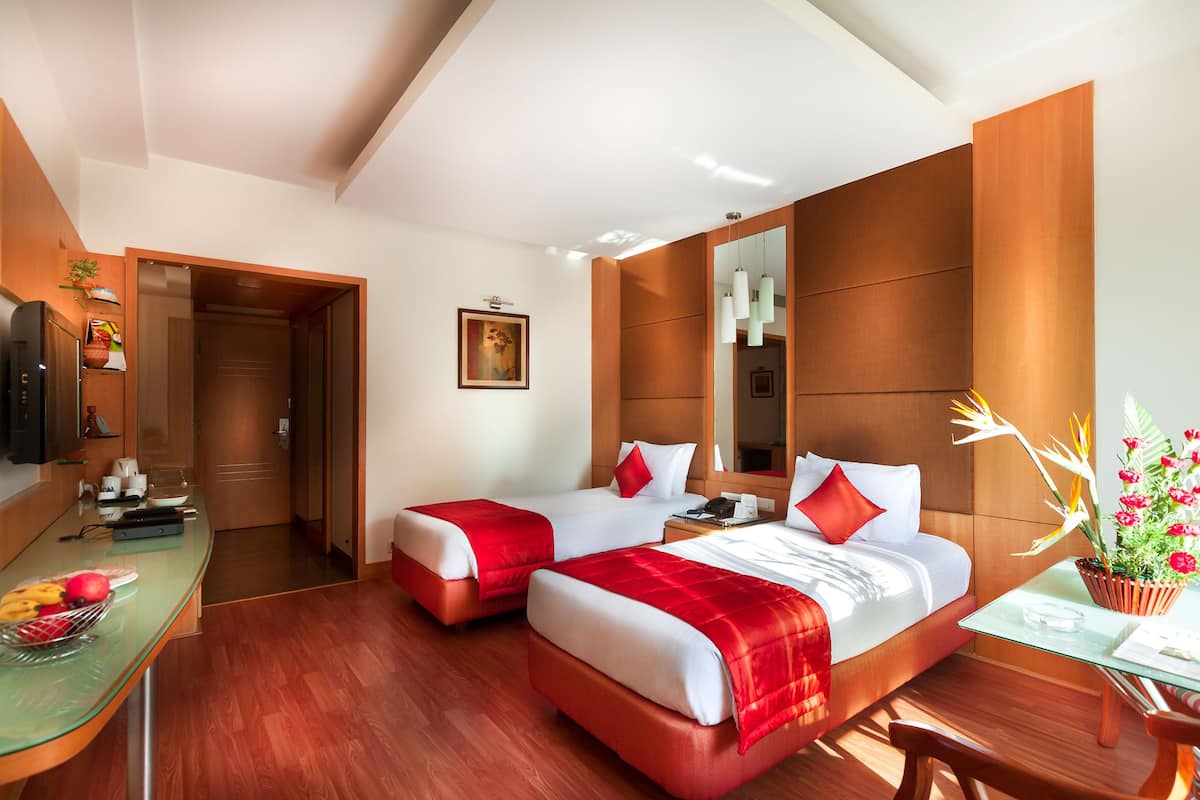 Habitación de hotel con dos camas, un escritorio con computadora, un espejo y una planta en maceta.