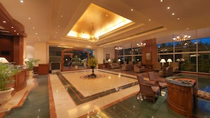 Eine großzügige Lobby mit einer zentralen Fontäne, einer Sitzecke und großen Fenstern mit Blick ins Freie.