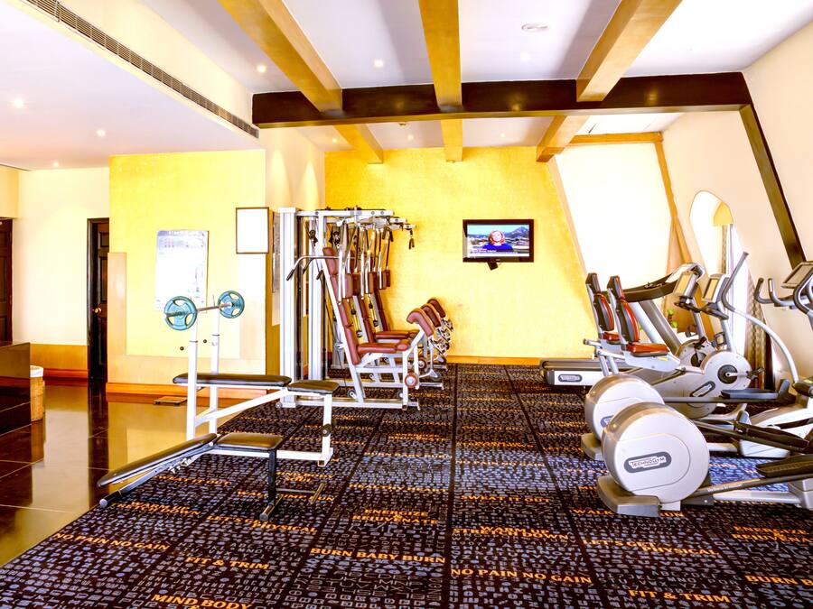 Un gimnasio con varios equipos de ejercicio, un televisor en la pared y un piso con diseño.