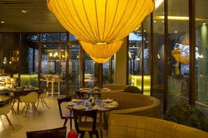 Uma zona de refeições moderna com um lustre grande e iluminado, paredes de vidro e diferentes opções de assento.