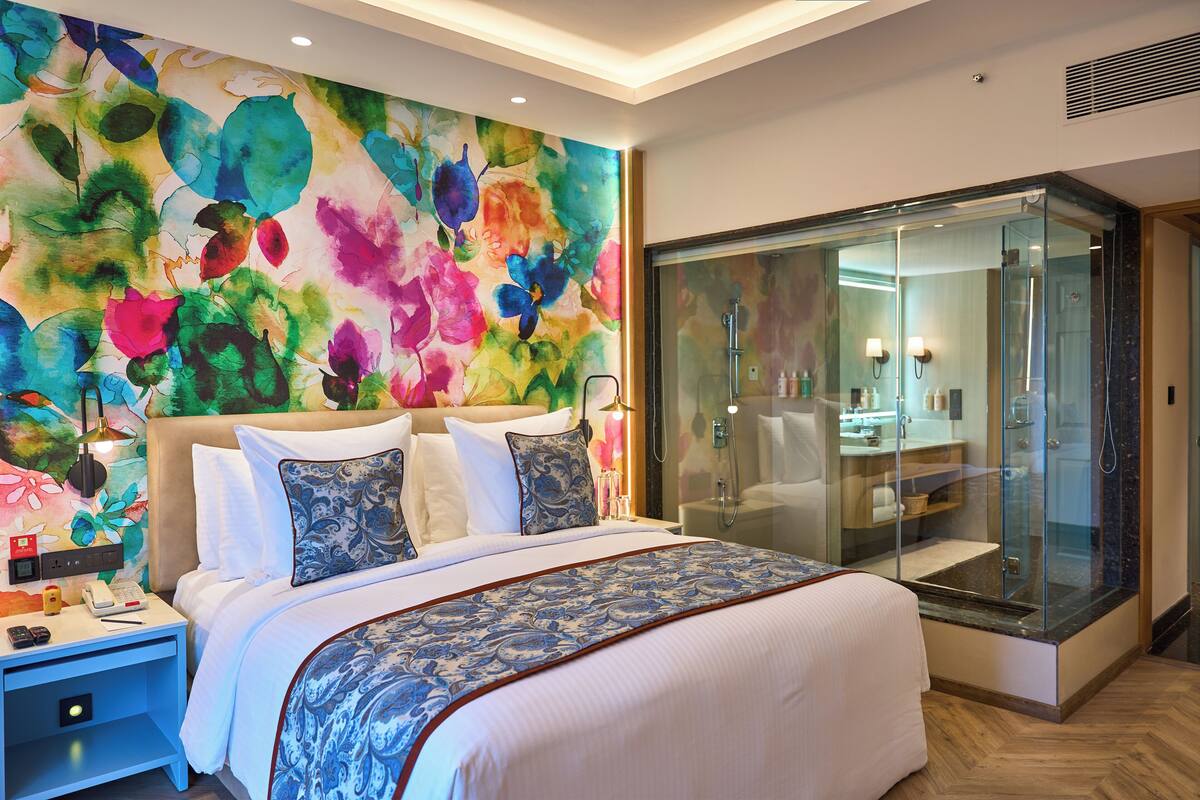 Een moderne hotelkamer met een groot bed, een douche met glazen wanden en een levendig bloemenwanddecor.