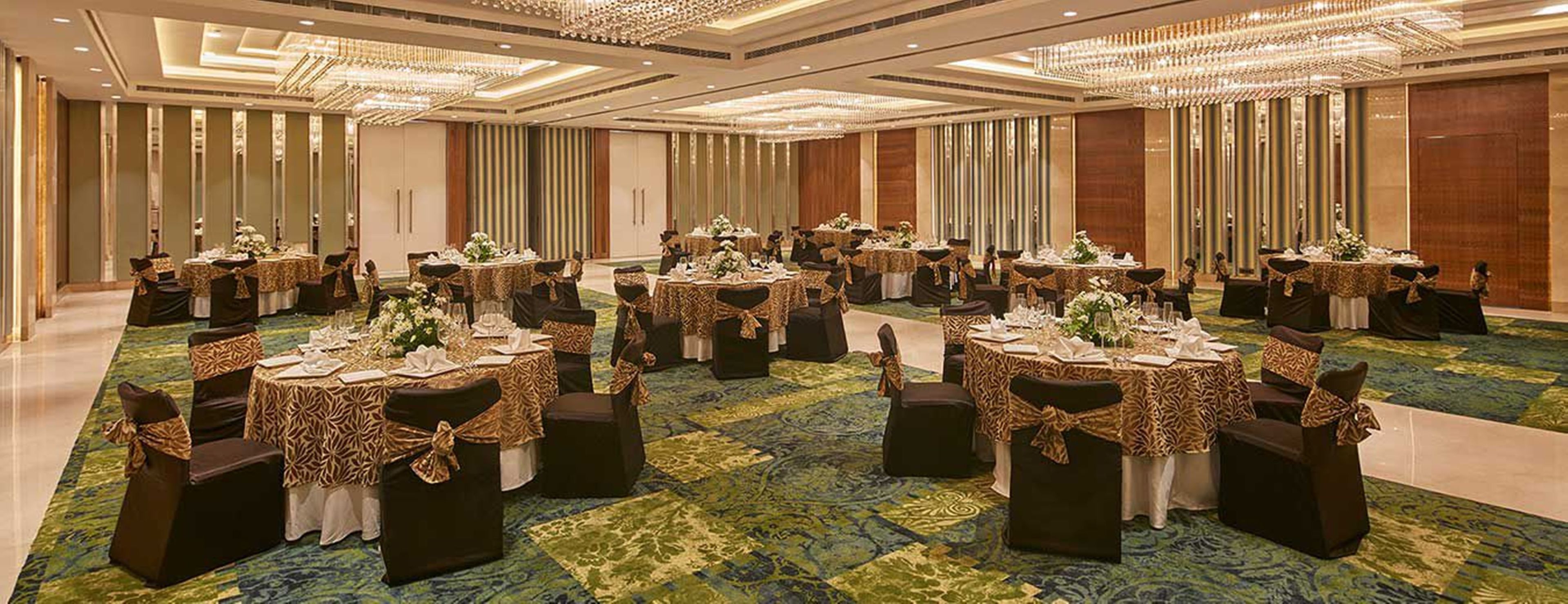 Un salón de banquetes con mesas redondas, sillas negras y cintas doradas.