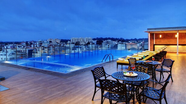 Ein Poolbereich auf dem Dach mit Blick auf die Stadt, Sitzgelegenheiten im Freien und einer Bar.