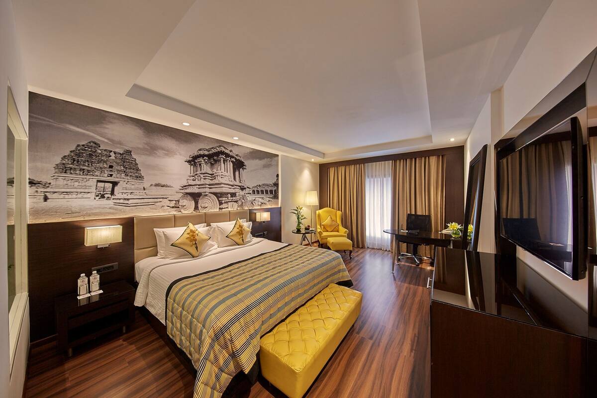 Een hotelkamer met een groot bed, een nachtkastje met een lamp, een stoel, een televisie en een muurschildering.