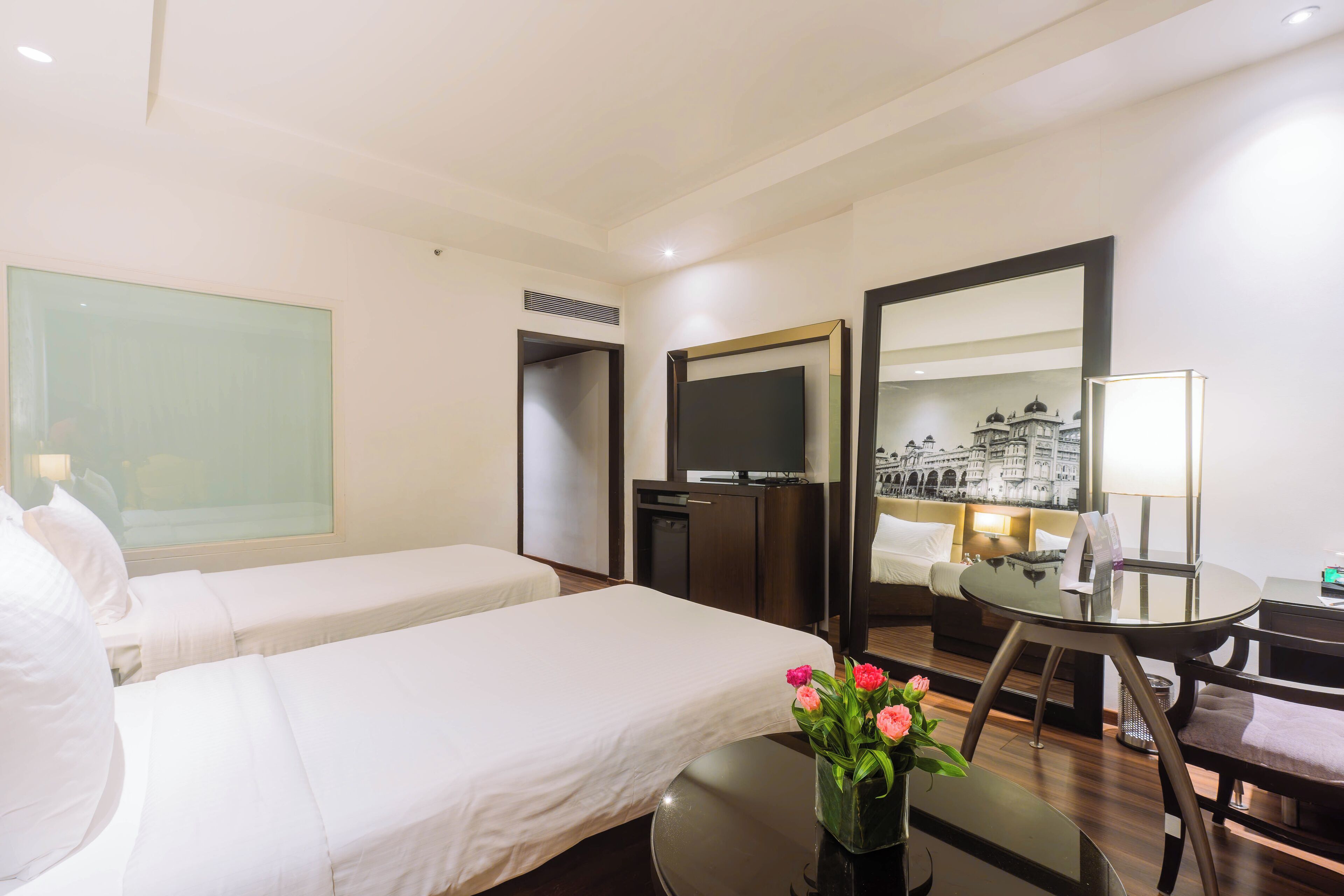 Une chambre d’hôtel avec deux lits, un bureau, une chaise, une télévision et un grand miroir.