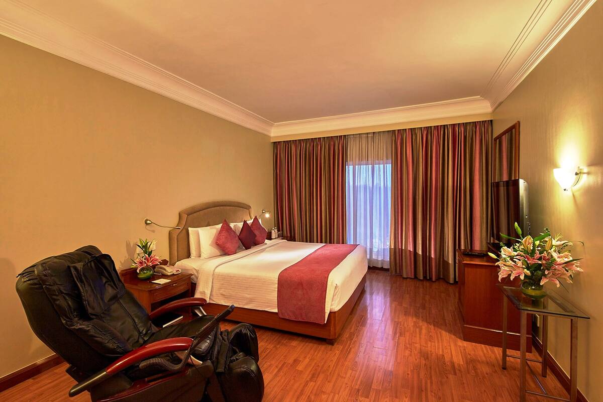 Een hotelkamer met een bed, een stoel, een bureau, een televisie en een bloemenvaas.