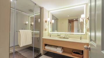 Un baño moderno con cabina de ducha de vidrio, un espejo grande con apliques de pared y un mueble de tocador de madera con perchero.