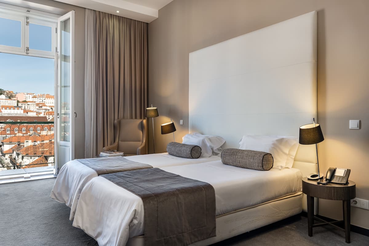 Habitación de hotel con una cama grande, dos mesitas de noche, una silla y vistas a la ciudad.