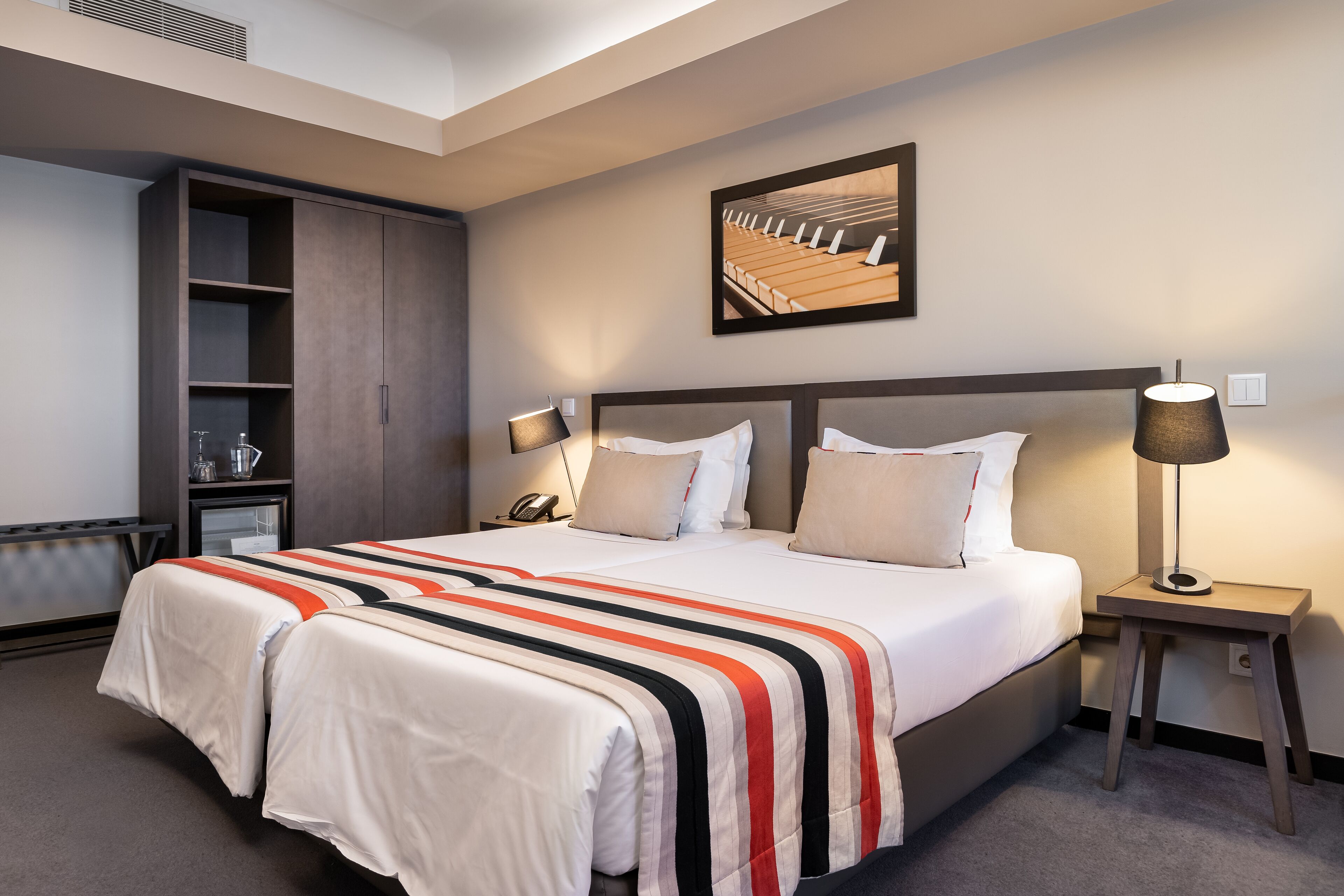 A hotel room with a large bed, a wardrobe, a bedside table with a lamp, and a painting on the wall.