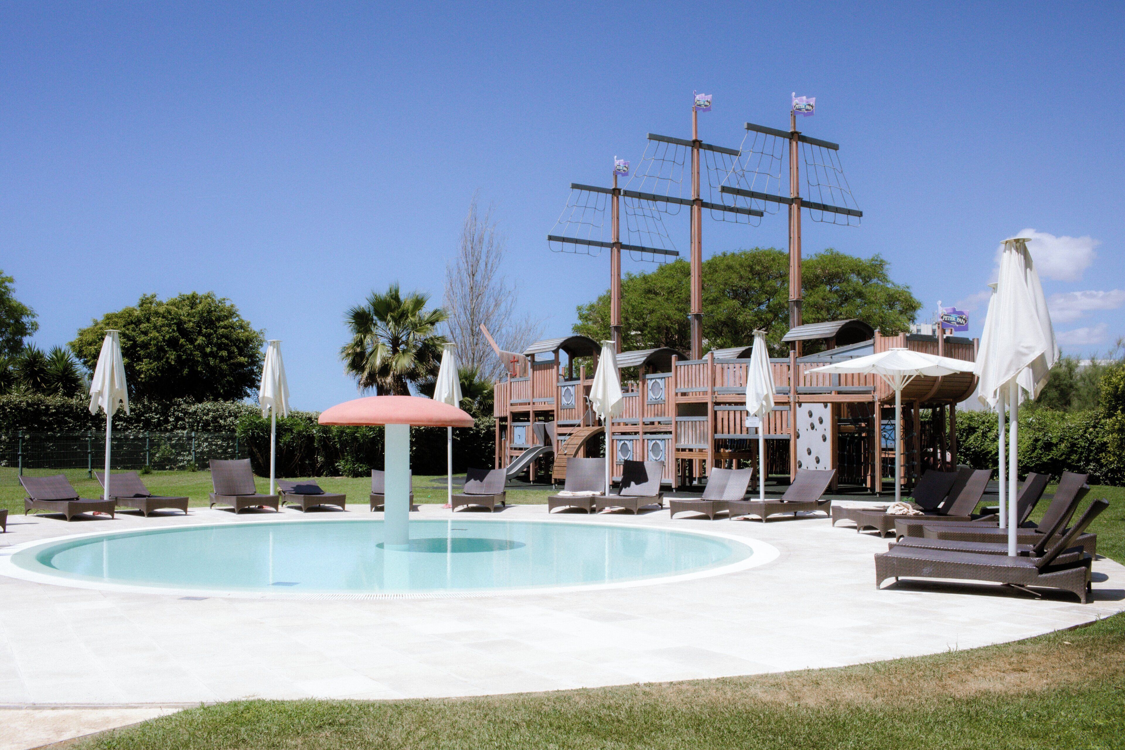 A pool area with lounge chairs, umbrellas, and a building with a ship-themed facade.