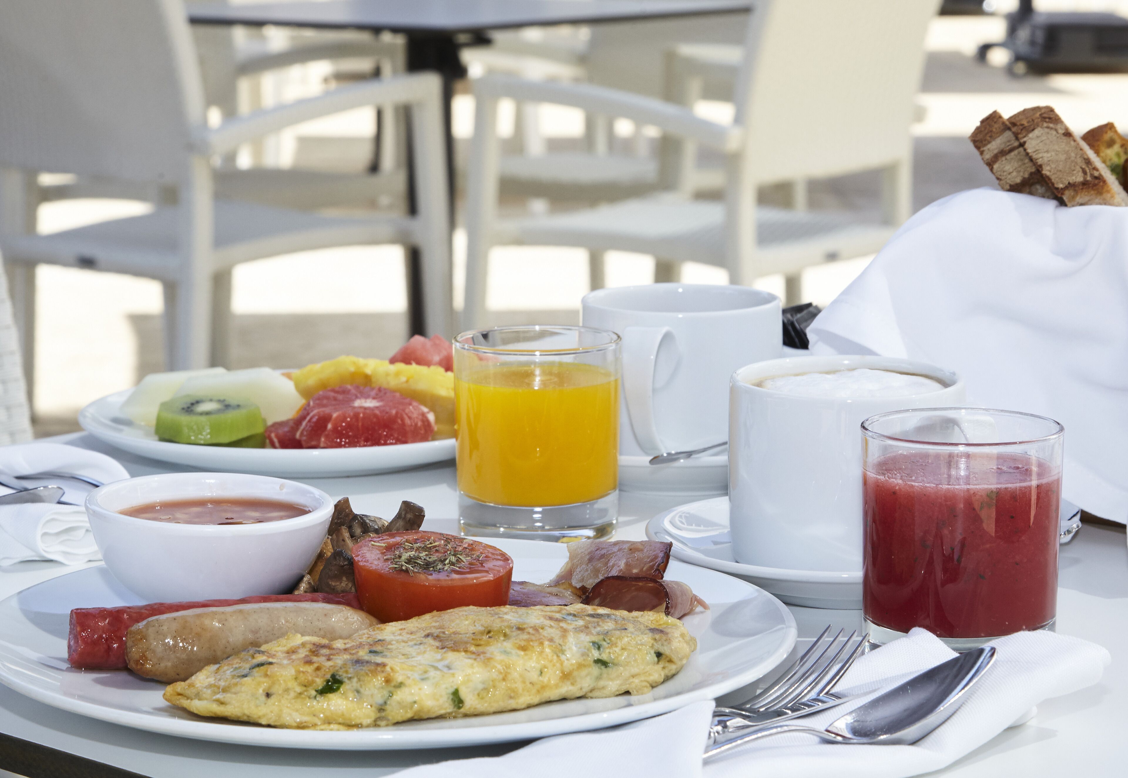 A breakfast table with plates of food, including eggs, bacon, and fruit, along with cups and glasses of beverages.