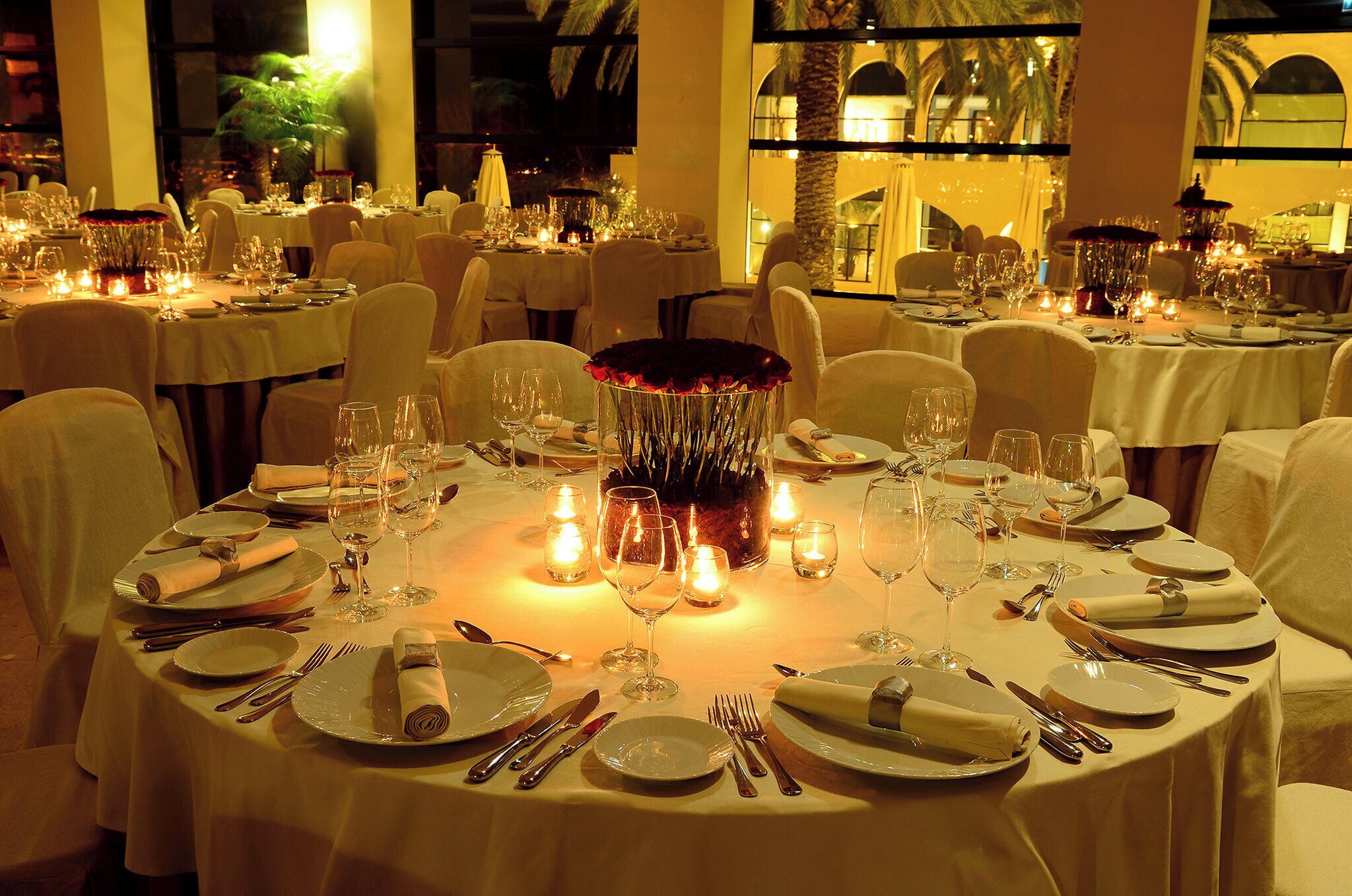 Un restaurant avec des tables rondes dressées pour le repas, chacune étant agrémentée d’assiettes, de couverts et de verres.
