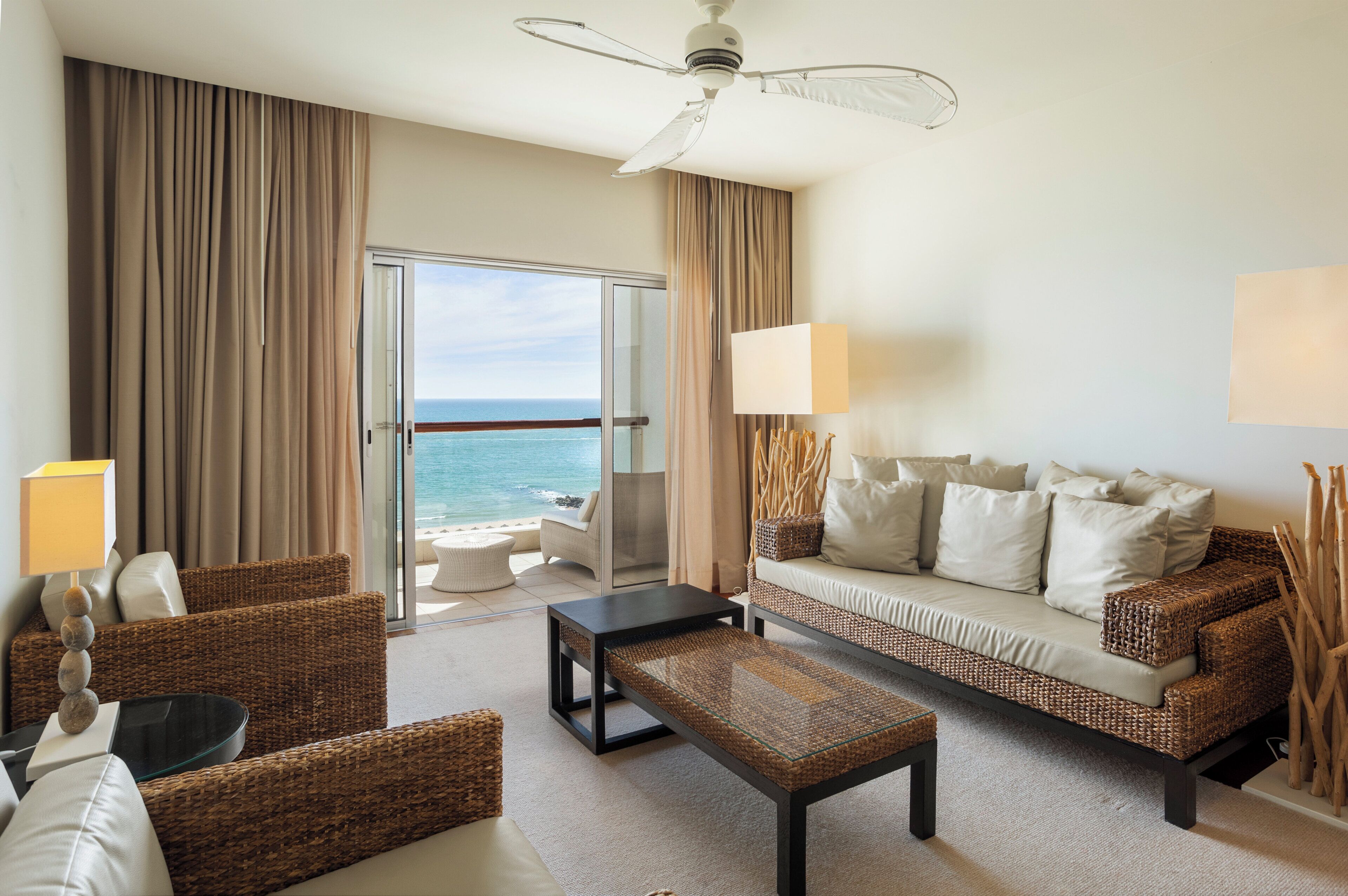 A hotel room with a balcony, a sofa, a coffee table, and a ceiling fan.