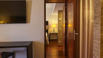 A hotel room with a flat-screen TV, a desk, and a chair. There is a wooden door leading to a bathroom with a sink and a mirror.