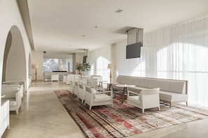 A spacious living area with a large sofa set, a patterned rug, and a flat-screen TV mounted on the wall.