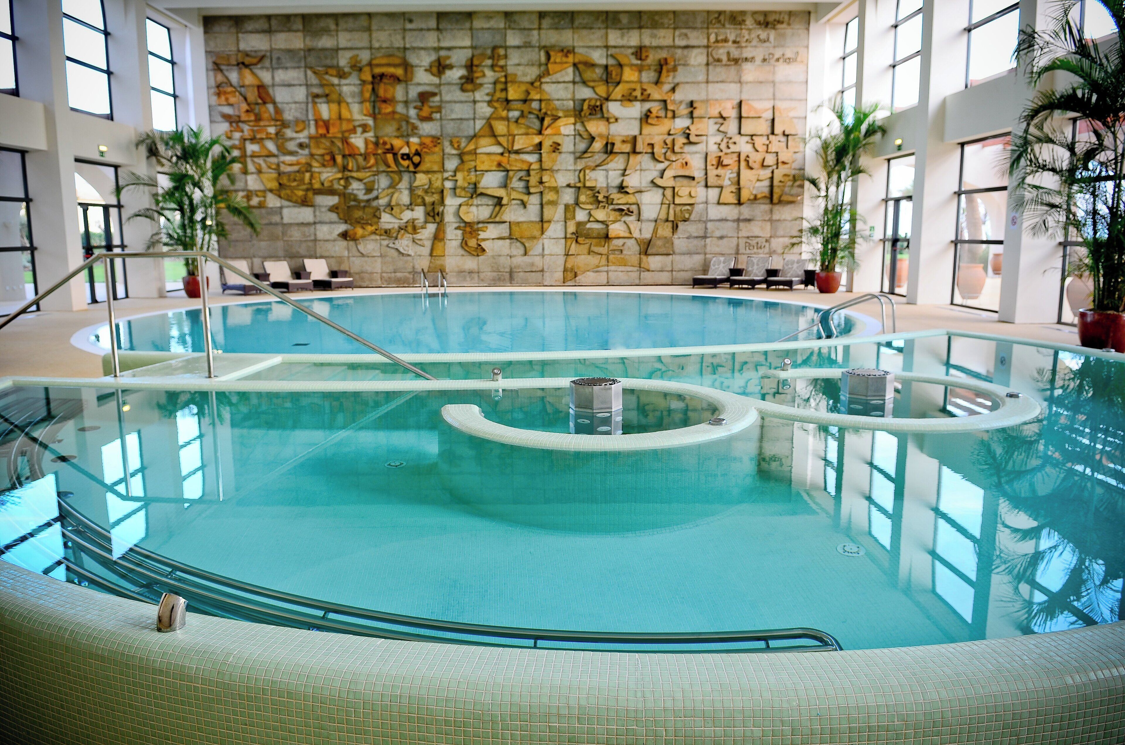 Una piscina interior con agua cristalina, rodeada de sillas de descanso y plantas en macetas.