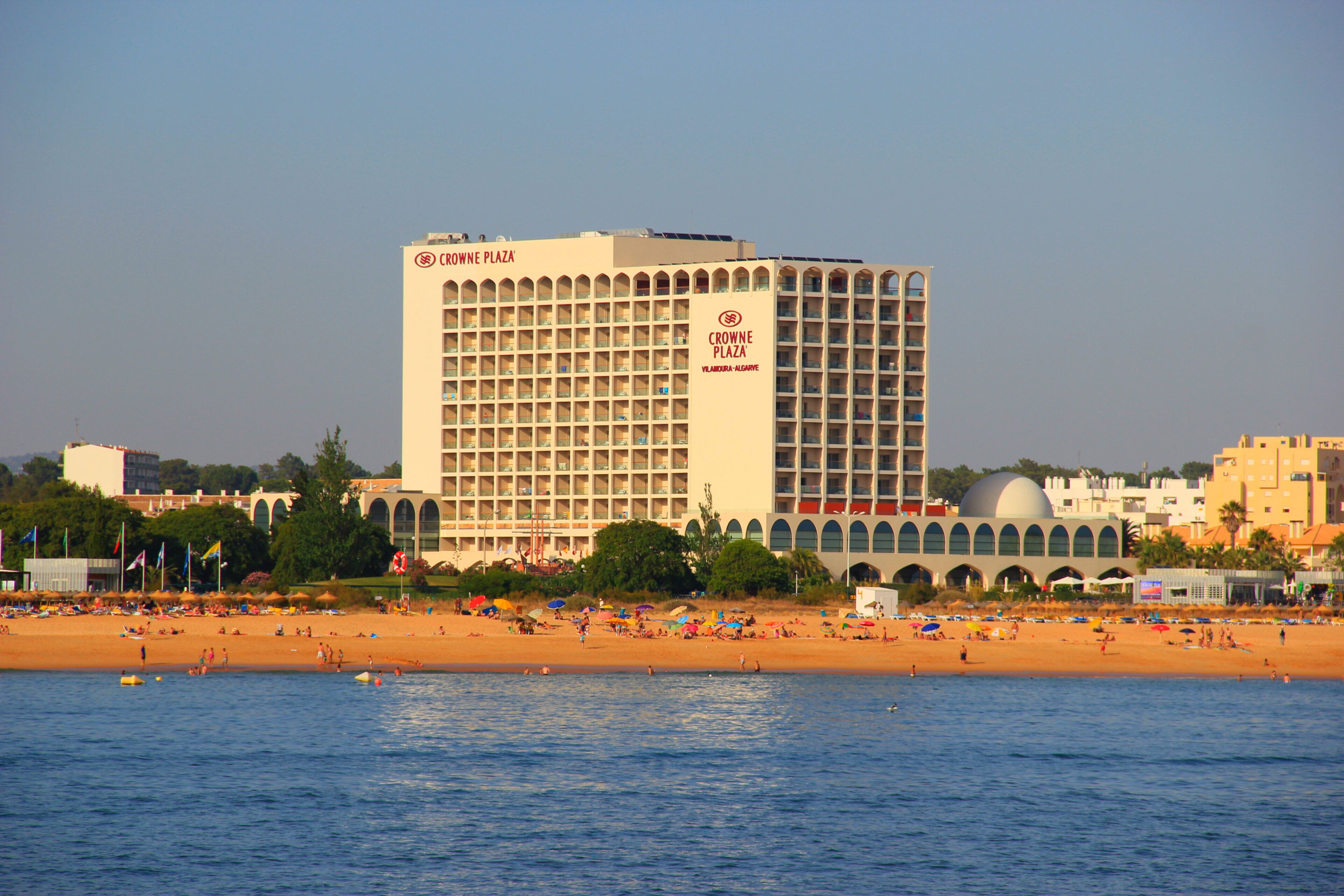 A hotel with a large number of balconies, a beach in the foreground, and a clear sky.