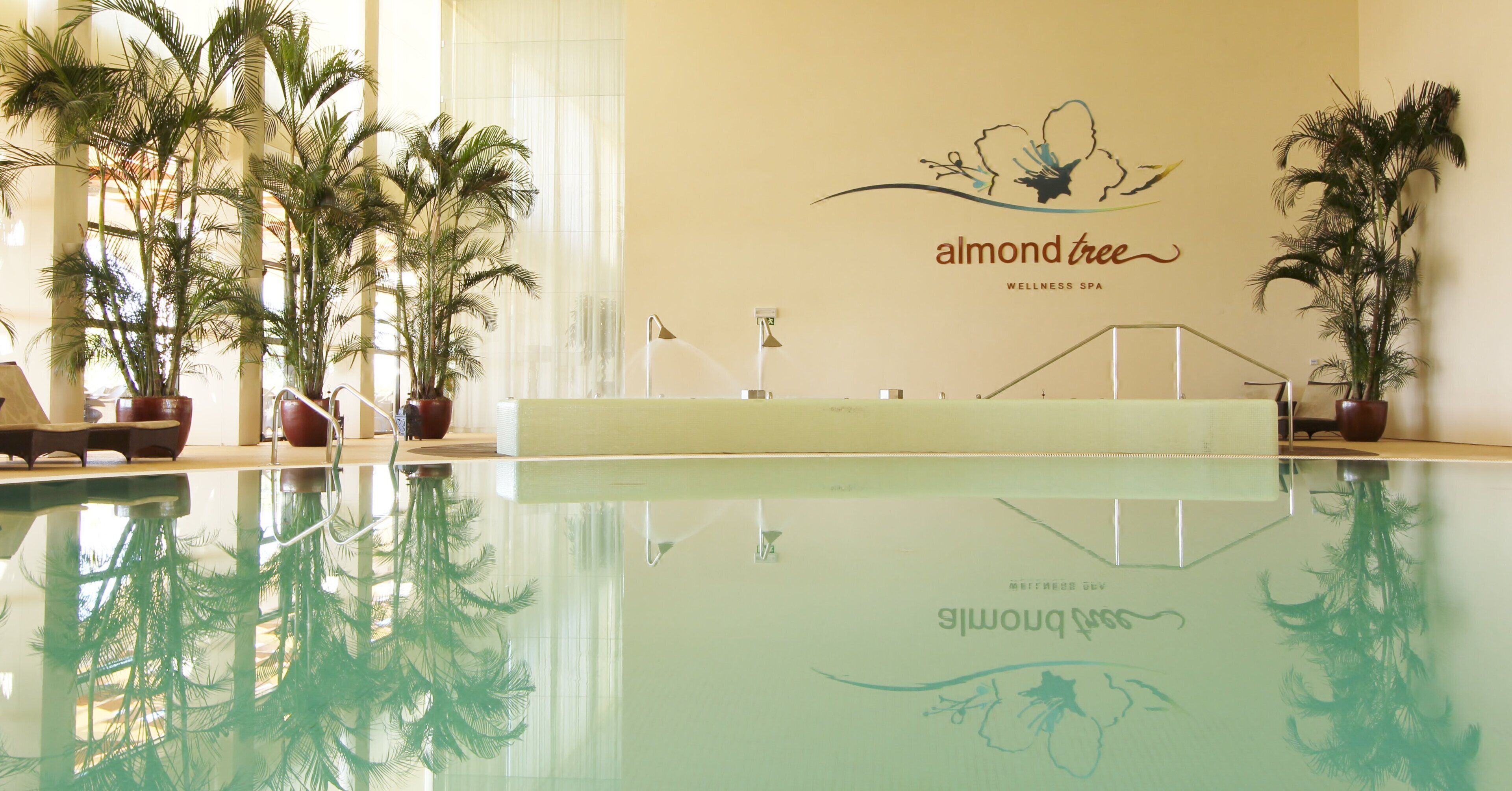 An indoor swimming pool with a wall featuring the text 'almond tree WELLNESS SPA' and a logo.