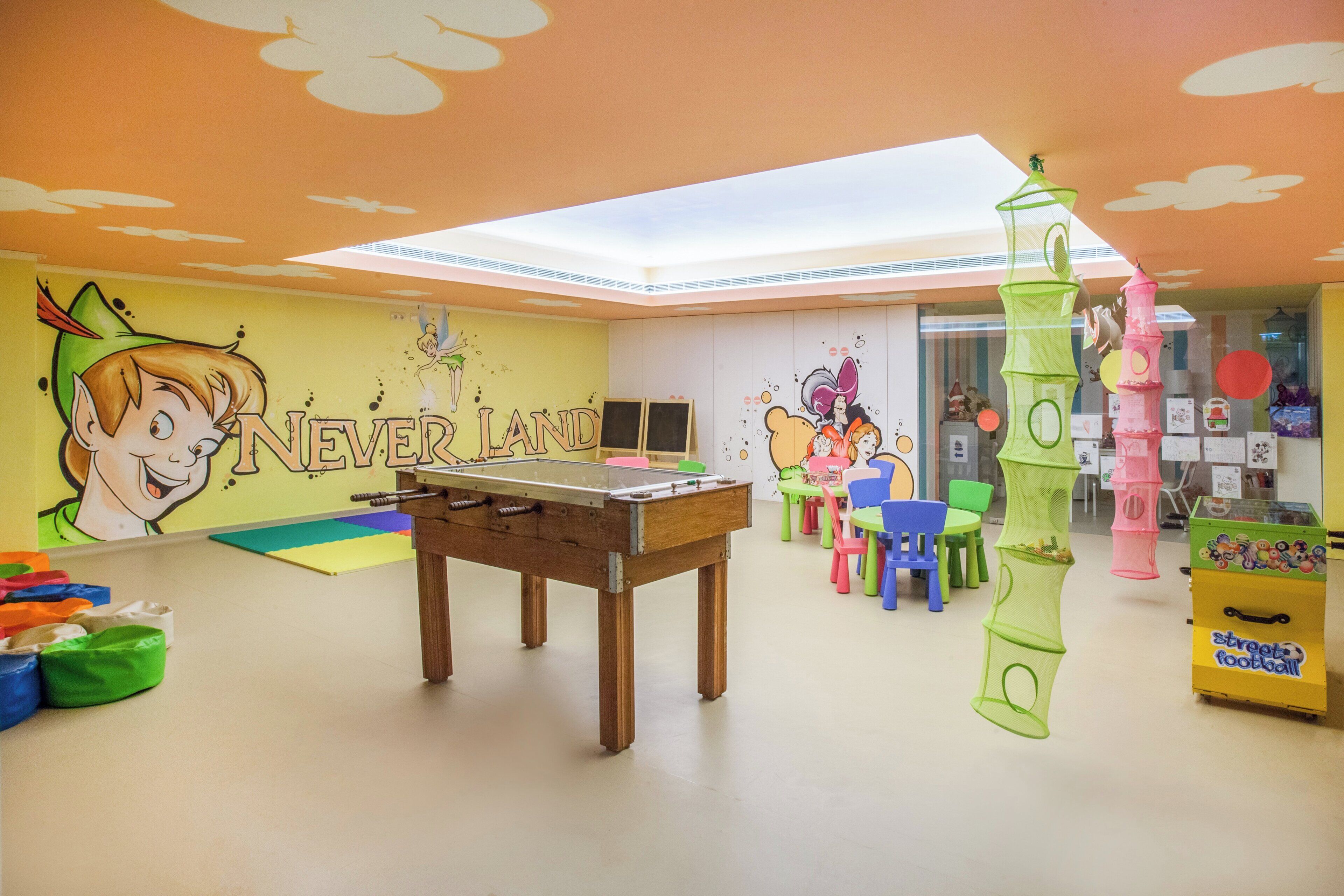A children's playroom with a foosball table, colorful chairs, and a mural.