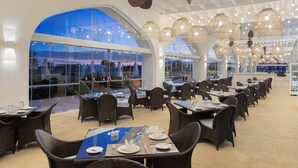 Un restaurante espacioso con techos altos, amplias ventanas arqueadas y mobiliario de mimbre.