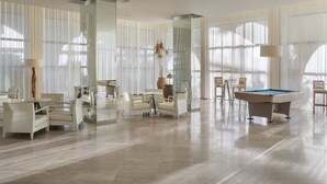 Un salón amplio y moderno con mesa de billar, asientos cómodos y grandes ventanales que permiten la entrada de luz natural.
