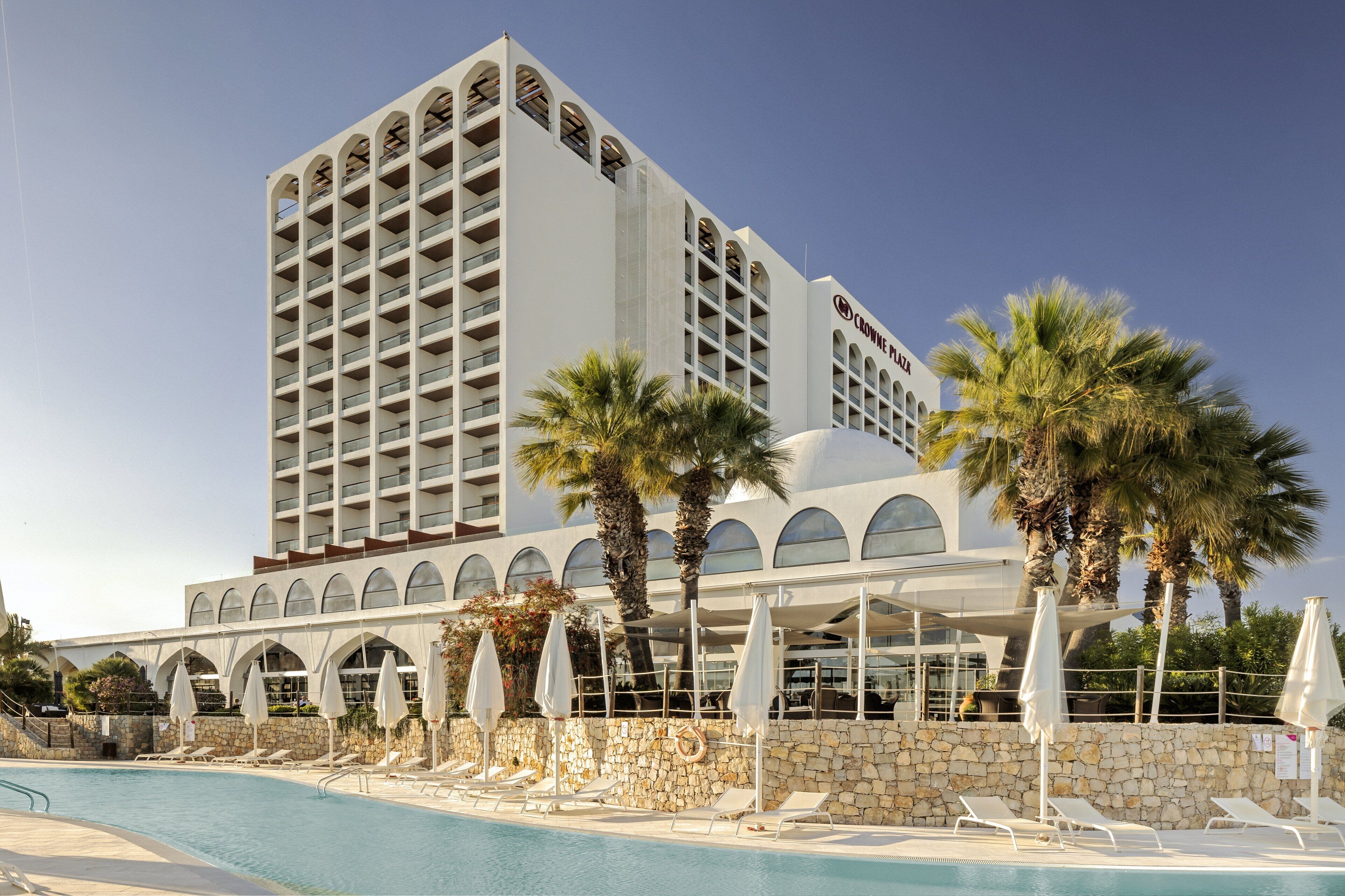 A hotel with a pool, palm trees, and a stone wall.