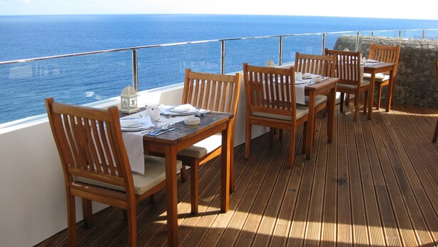 A wooden deck with a table set for dining, overlooking the ocean. - Madeira Regency Cliff (Funchal)