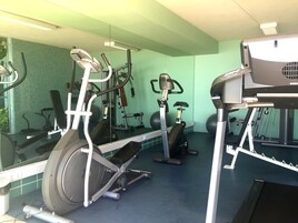 Ginásio com equipamentos de exercício, espelho e parede verde.
