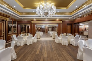A banquet hall with wooden flooring, white chairs, and tables set for a formal event. - Radisson Hotel Jalandhar Grand Windsor Resorts Ltd (Jalandhar)