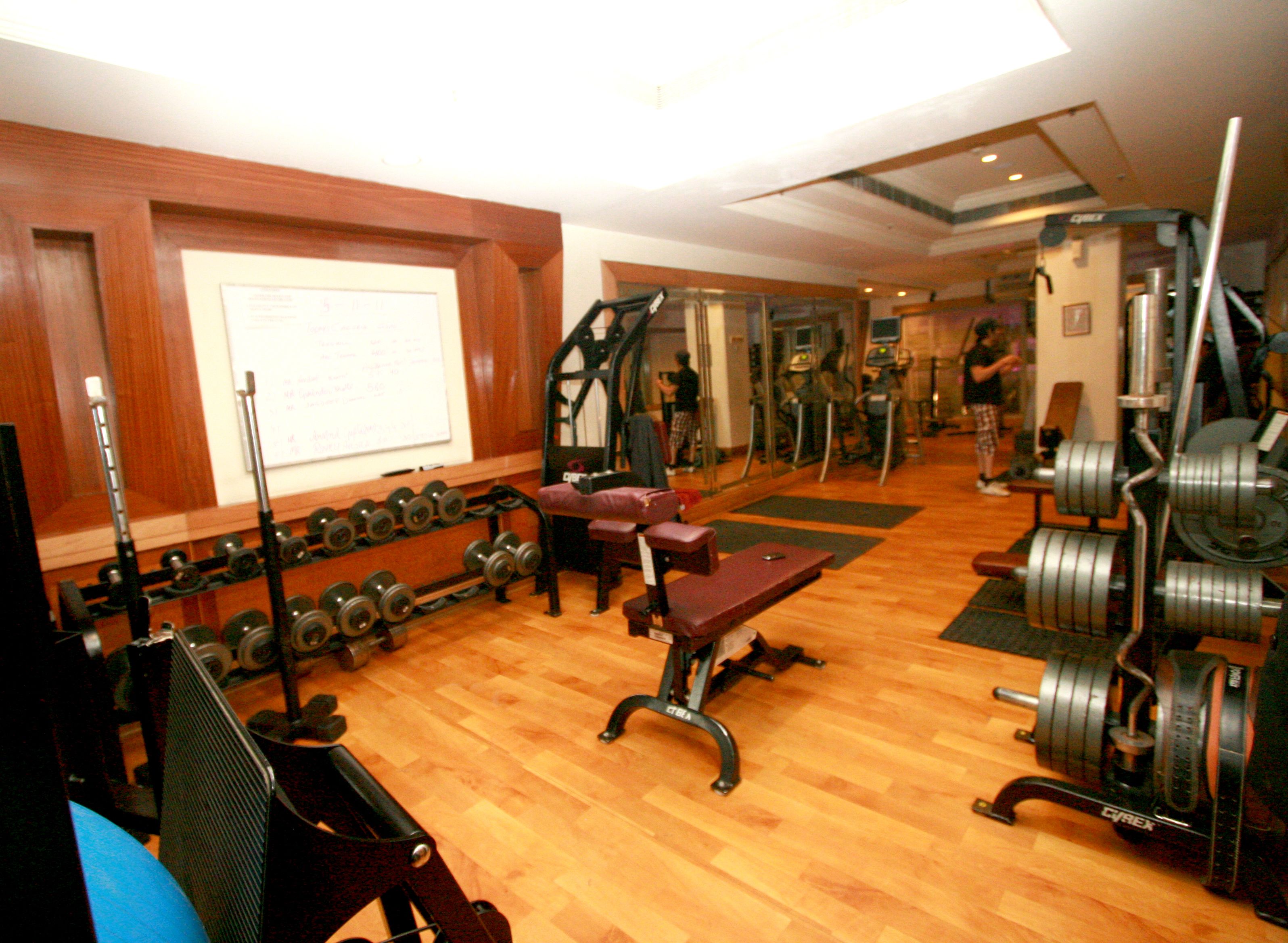 Uma academia com diversos equipamentos de ginástica, incluindo halteres, um banco e aparelhos de cardio.