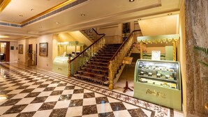 Eine prachtvolle Hotelhalle mit einem Schachbrettmuster aus Marmor, einer imposanten Treppe mit aufwendiger Balustrade und einer Vitrine mit Gebäck.