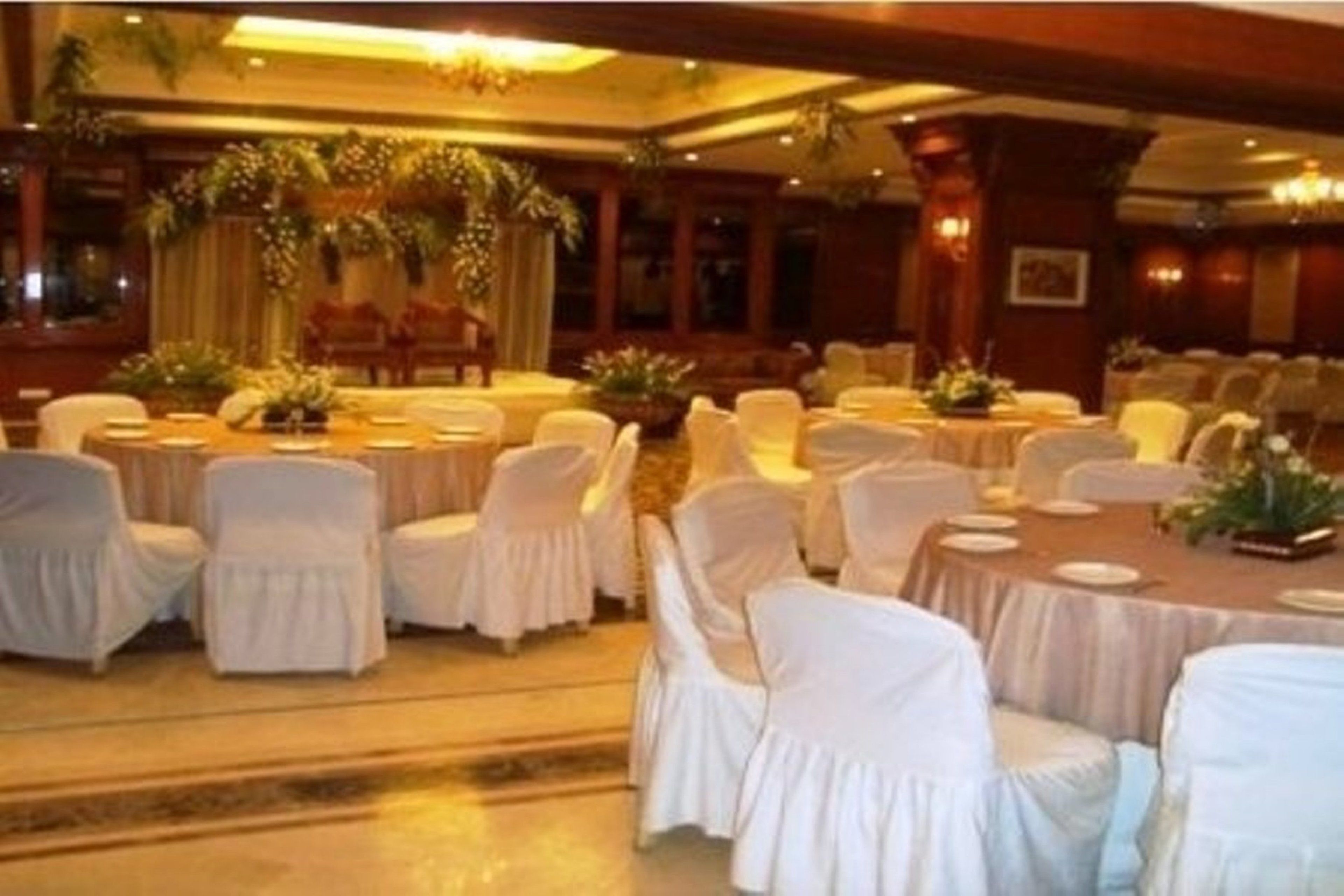 A banquet hall with round tables, white chairs, and floral centerpieces.