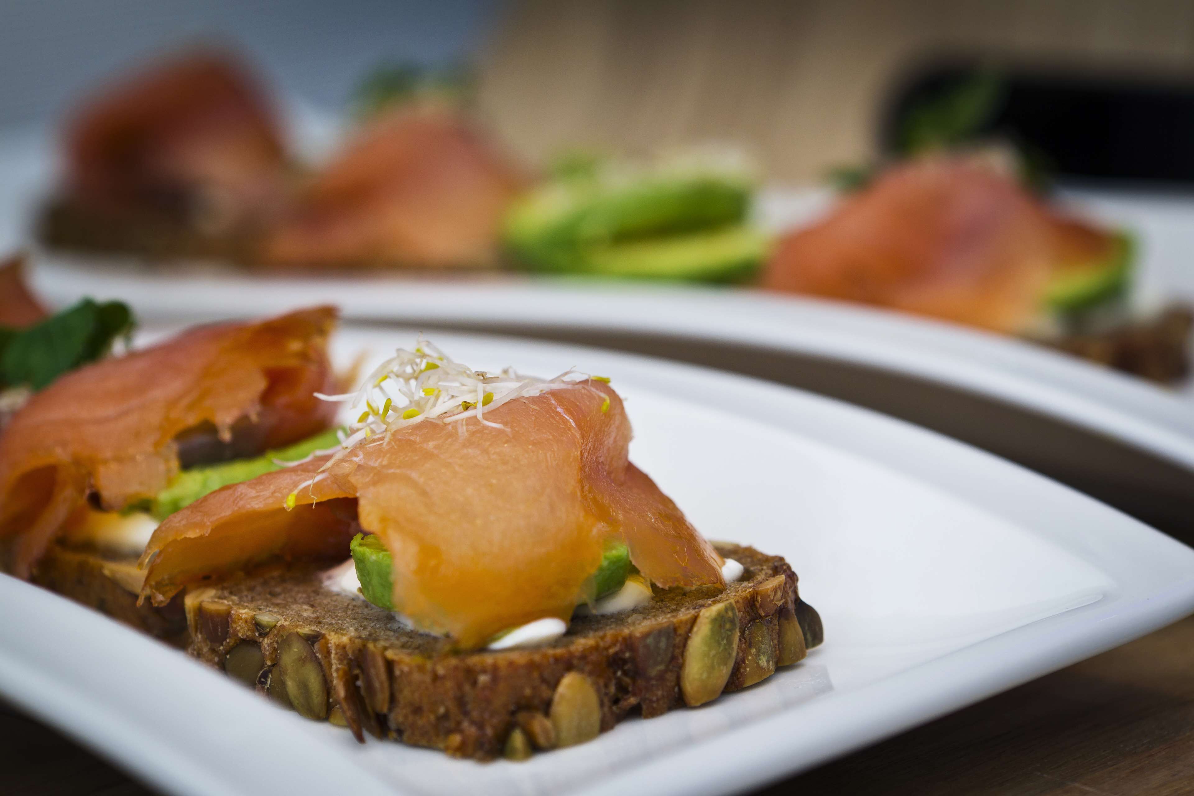 A plate with a slice of bread topped with salmon and avocado, garnished with seeds.