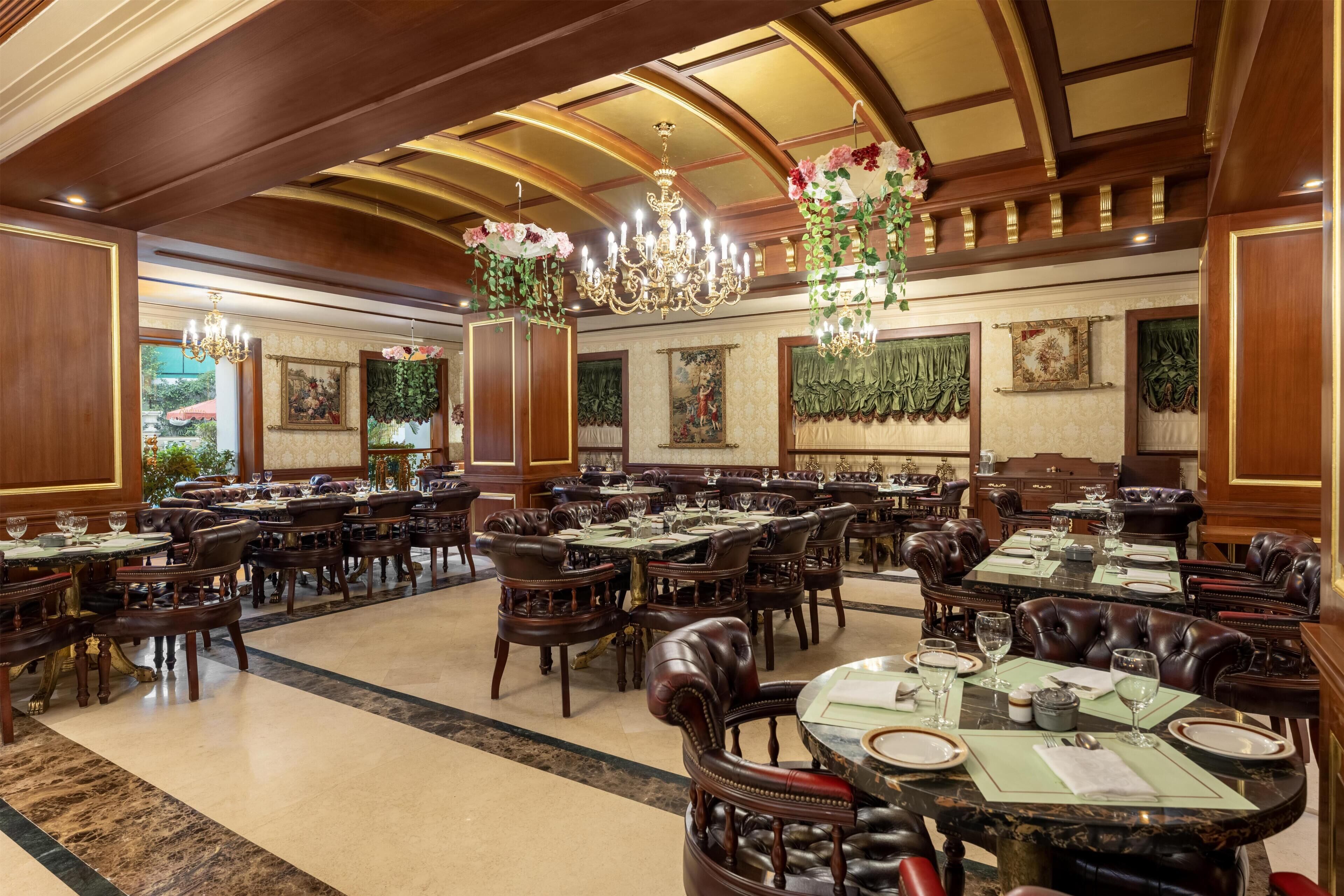 Uma sala de jantar formal com várias mesas e cadeiras, lustres e quadros nas paredes.