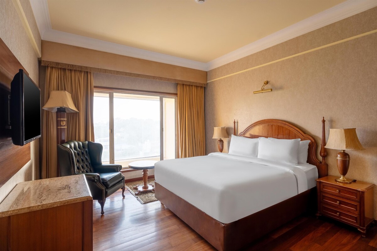 A hotel room with a large bed, a desk, a chair, a television, and a window with curtains.