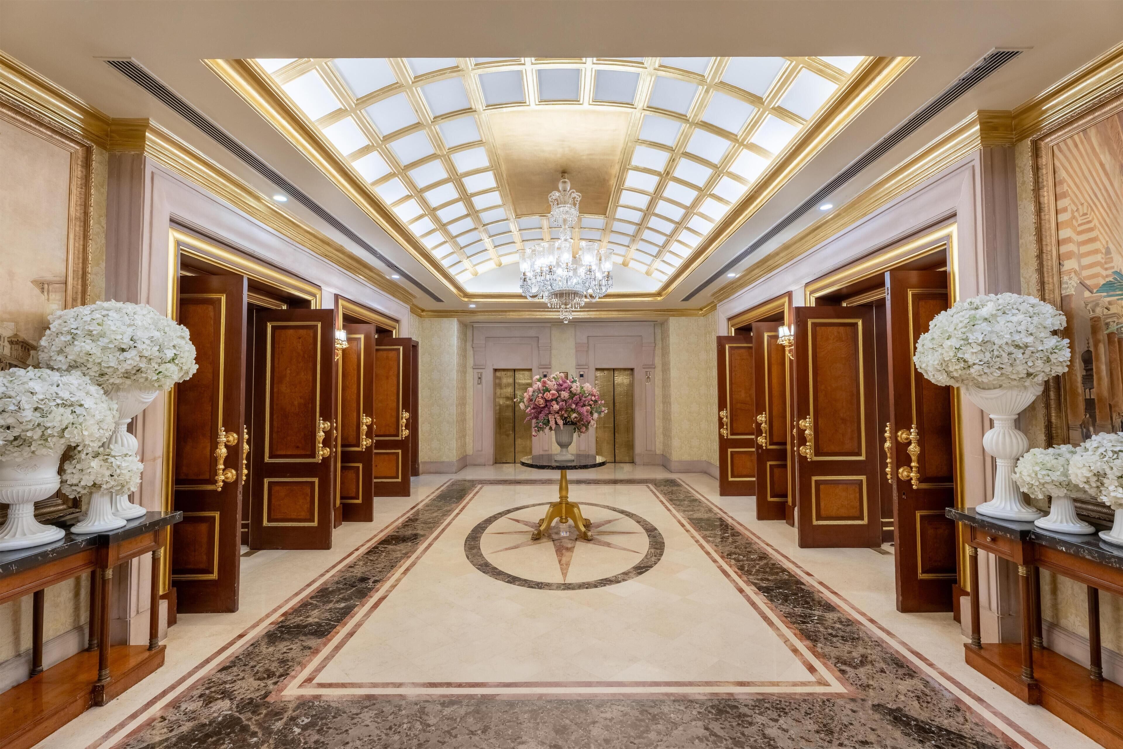 Un amplio pasillo con techo alto, puertas ornamentales y un candelabro central.