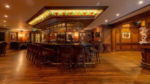 Eine Bar mit einer Decke aus Buntglas, einer Holztresore und mehreren Barhocker.