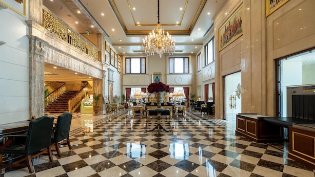Eine geräumige Lobby mit Schachbrettmuster-Boden, einem imposanten Kronleuchter und einer Treppe, die in eine obere Ebene führt.