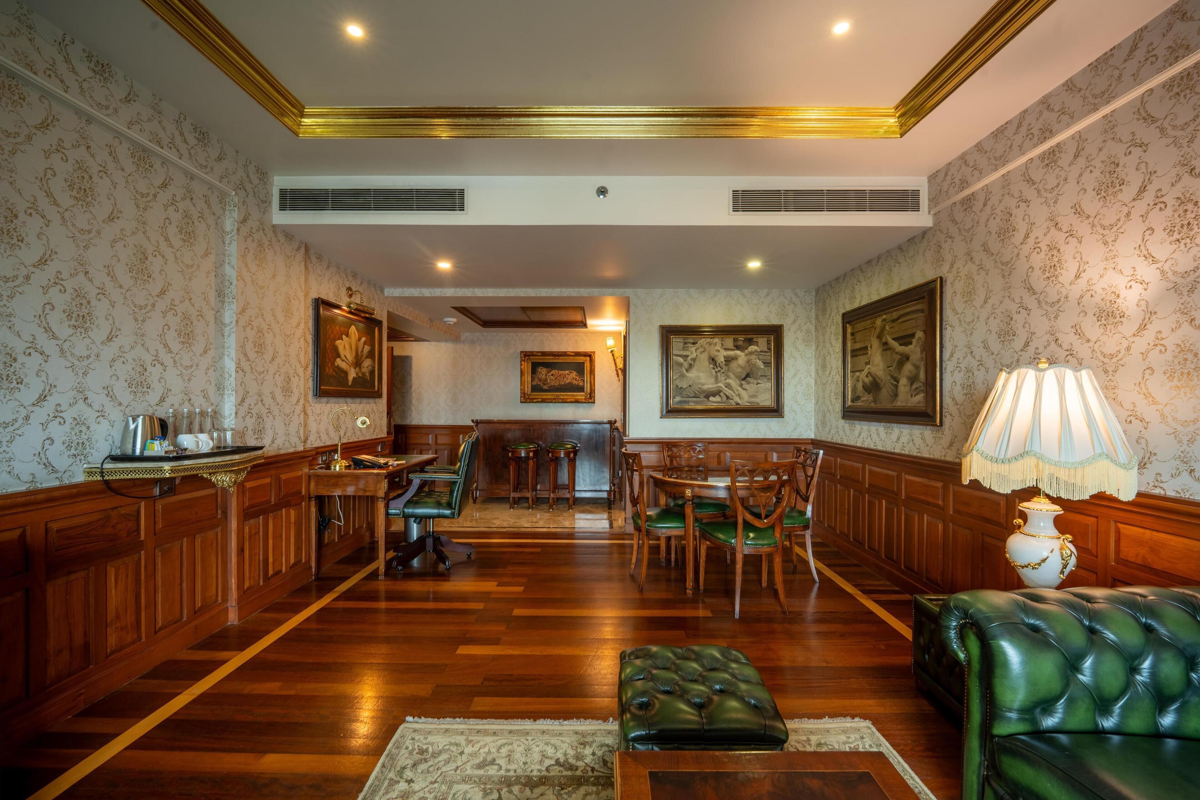 A spacious room with wooden paneling, a green leather sofa, a dining area with chairs, and a table.