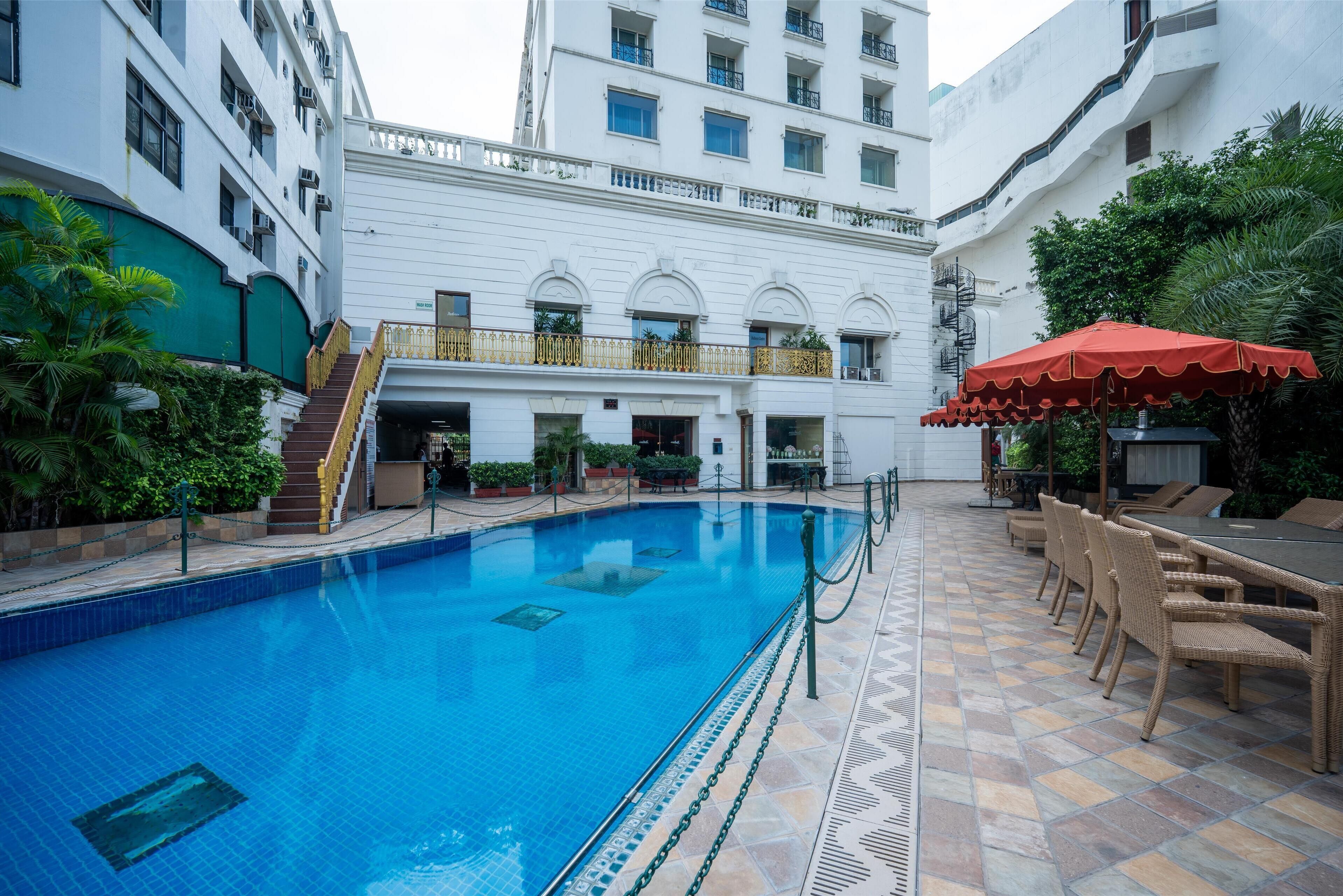 A swimming pool with a tiled deck, surrounded by lounge chairs and a red umbrella.