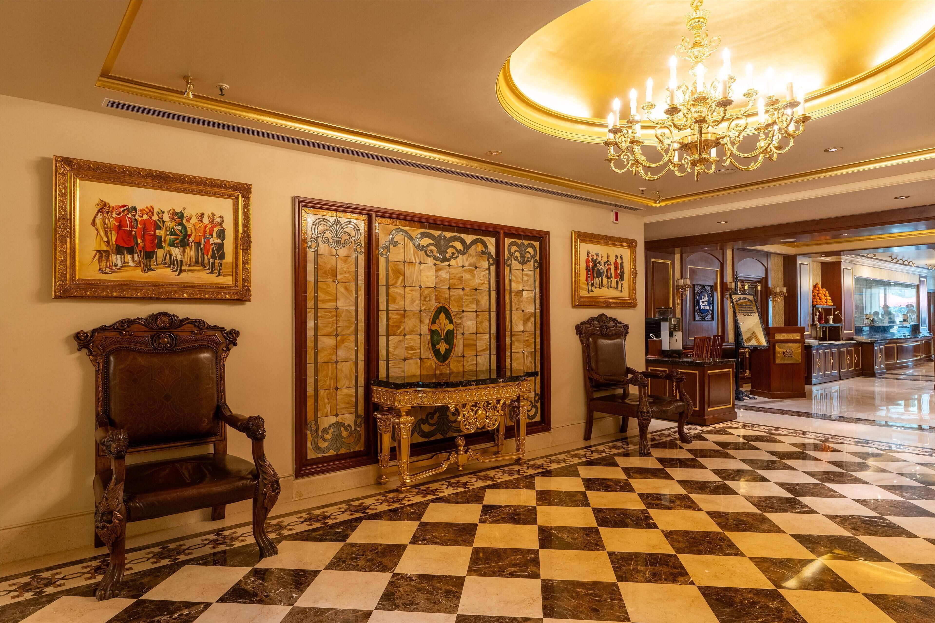 A lobby with a checkered floor, ornate chairs, a grand chandelier, and framed artwork on the walls.