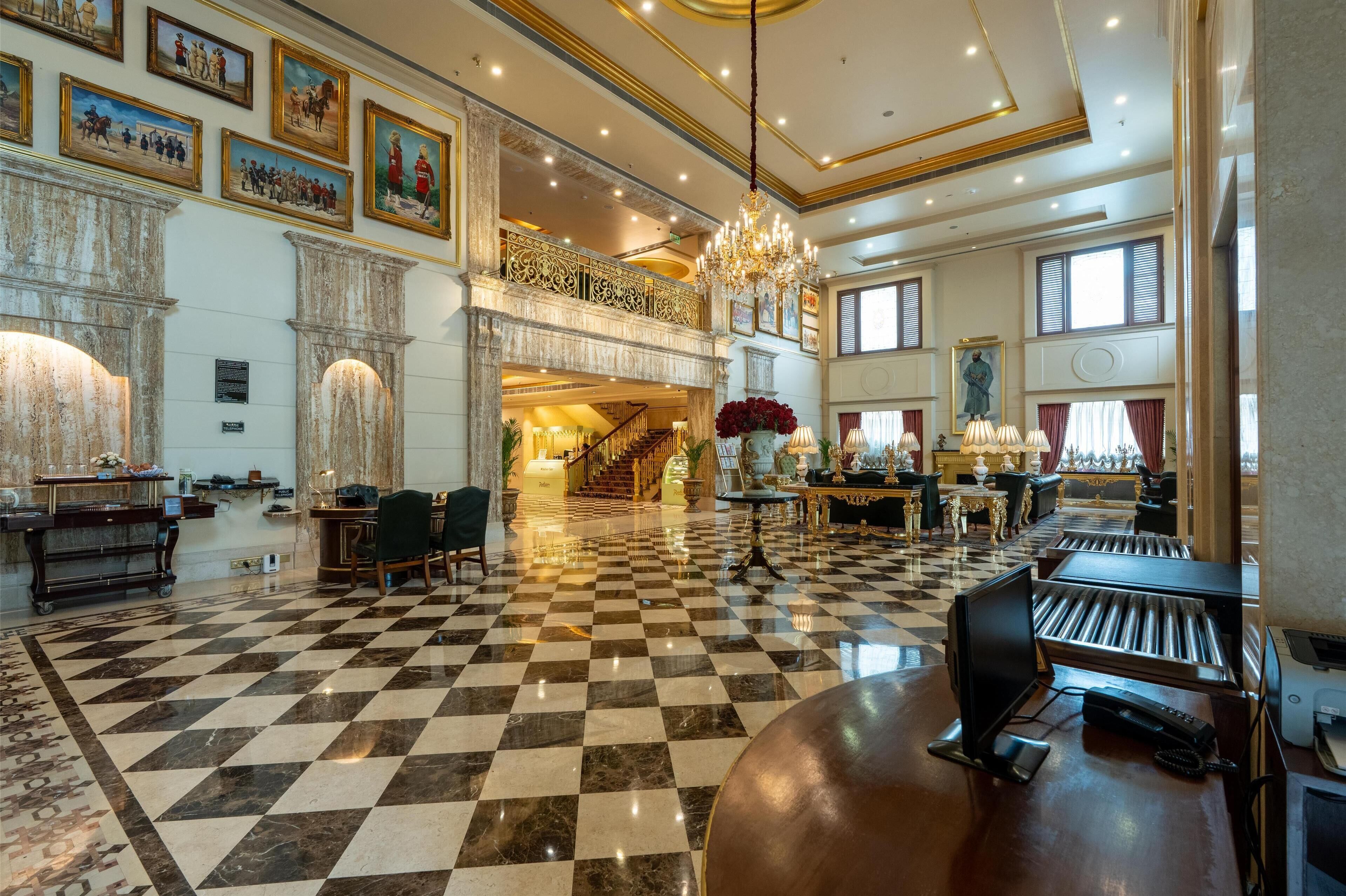 A spacious lobby with a checkered floor, a grand staircase, and a chandelier.
