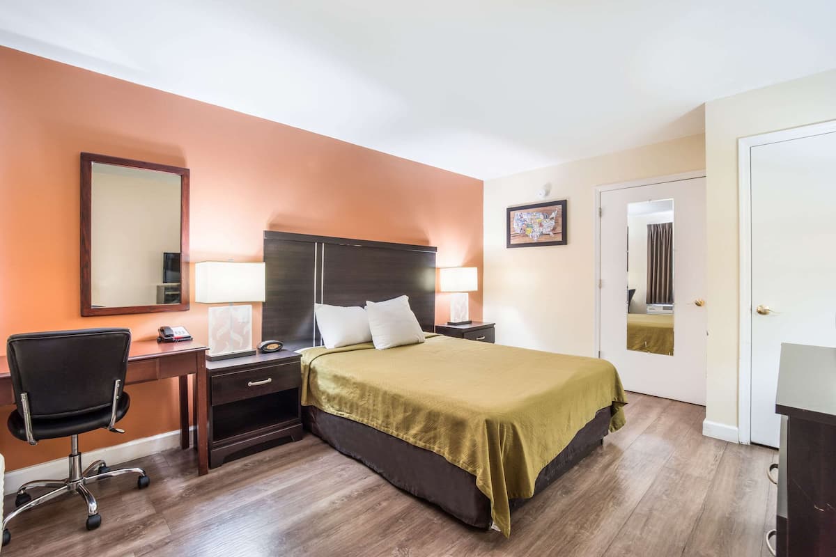 A hotel room with a bed, desk, chair, and a door.